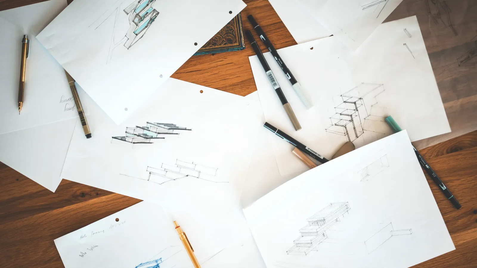Architectural sketches, pens and markers arranged across a wooden worktable.